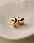small, polished gold crescent-shaped stud earring against a light gray background.