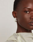 Close-up of a model wearing a single silver-toned geometric stud earring with a polished rectangular bar design.