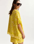Woman wearing a yellow patterned cover-up with fringe on a white background