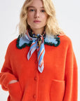 Person wearing an orange cardigan with a colorful scarf on a white background