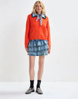 Person wearing an orange cardigan, denim skirt, and patterned scarf on a white background