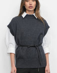 Woman wearing a dark gray sleeveless sweater vest over a white shirt on a white background