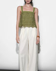 Woman wearing a green top and white pants against a white background