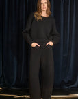 Woman wearing a black outfit against a dark blue curtain background