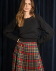 Woman wearing a black sweater and red plaid skirt against a dark background