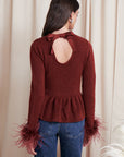 Woman wearing a burgundy sweater with feather details and blue jeans against a beige curtain background, back