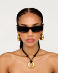 Woman wearing black sunglasses, gold hoop earrings, and a gold necklace on a white background