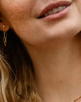 Close-up of a person wearing gold earrings and a necklace with a blurred background.