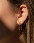 Close-up of an ear wearing gold chain earrings with a blurred background