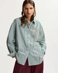 Woman wearing a green and white striped shirt with floral embellishments on a white background