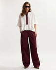 Woman wearing a white blouse with a maroon collar and burgundy pants on a white background