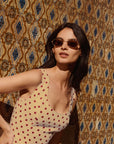 Woman wearing a polka dot dress and sunglasses against a patterned wall.