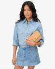 Woman wearing a denim outfit holding a beige handbag on a white background