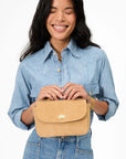 Woman holding the top handle of a tan crossbody bag against a white background