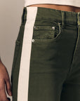 Close-up of olive green denim jeans with a wide off-white vertical stripe running down the side, worn by a model.