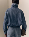 model wearing a denim jacket with jeans on a cream background, back view