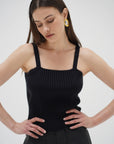 Woman wearing a black sleeveless top with yellow earrings on a white background front view