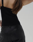 Person wearing a black ribbed tank top and black pants against a plain background back view