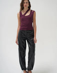 A model stands against a light gray studio background wearing a sleeveless deep purple top with a crossover neckline and black shiny cropped pants with drawstring ankle ties.