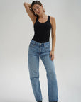 Woman wearing a black tank top and blue jeans on a plain background front view