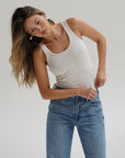 Woman wearing a white tank top and blue jeans against a plain background