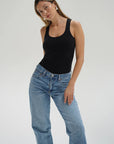 Woman wearing a black tank top and blue jeans on a plain background front view