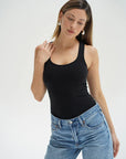 Woman wearing a black tank top and blue jeans on a white background front view