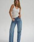Woman wearing a white tank top and blue jeans on a plain background front view