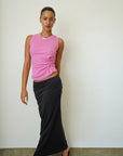Woman wearing a pink sleeveless top and black skirt against a white wall.