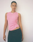 Woman wearing a pink sleeveless top and green skirt against a plain background