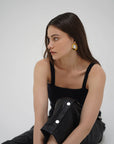 Woman wearing a black dress with silver buttons against a white background front view