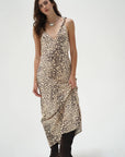 A woman modeling a sleeveless beige slip dress with a black leopard print pattern, paired with black boots, against a plain light gray studio background.