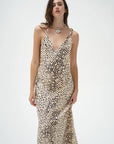 A woman modeling a sleeveless V-neck maxi dress with a beige and black leopard print pattern, set against a plain light gray studio background.