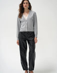 A woman modeling a light gray button-up cardigan, black shiny cropped pants, and black pointed shoes against a plain light gray studio background.