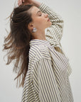 Woman wearing a striped shirt with her hair blowing in the wind against a plain background side view