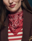 Person wearing a red bandana with white patterns over a striped shirt and brown jacket.