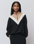 Woman wearing a black and beige color-blocked sweater against a plain background