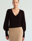 A model wearing a dark brown long-sleeve wrap top with balloon sleeves and a beige knit pencil skirt, photographed against a light gray studio background.
