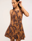 A woman modeling a sleeveless brown and black leopard-print mini dress with a button-down front, photographed against a plain light background.