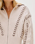 Beige sweater with intricate cable knit pattern on a white background