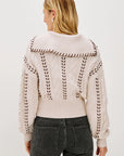 Person wearing a cream-colored sweater with intricate back design on a white background