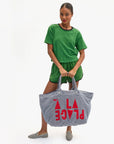 Woman holding a striped tote bag with 'PLeASe' text against a white background