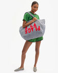 Woman holding a large striped bag with 'PLAGE' text on a white background