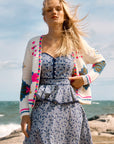 Woman wearing a colorful cardigan over a patterned dress on a beach.