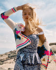 Woman wearing a colorful cardigan and patterned dress standing on a rocky beach.