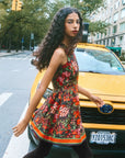 Woman in a floral dress crossing a street with a yellow taxi in the background