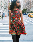 Woman in a colorful floral dress standing on a city street.