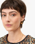 Close-up of a person with short hair wearing gold earrings and a necklace on a white background