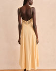 Woman wearing a yellow dress with lace detailing on a beige background, back