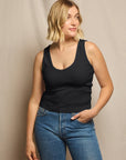 Woman wearing a black tank top and blue jeans against a beige background, size L